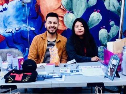 Two individuals sitting at a table selling jewelry